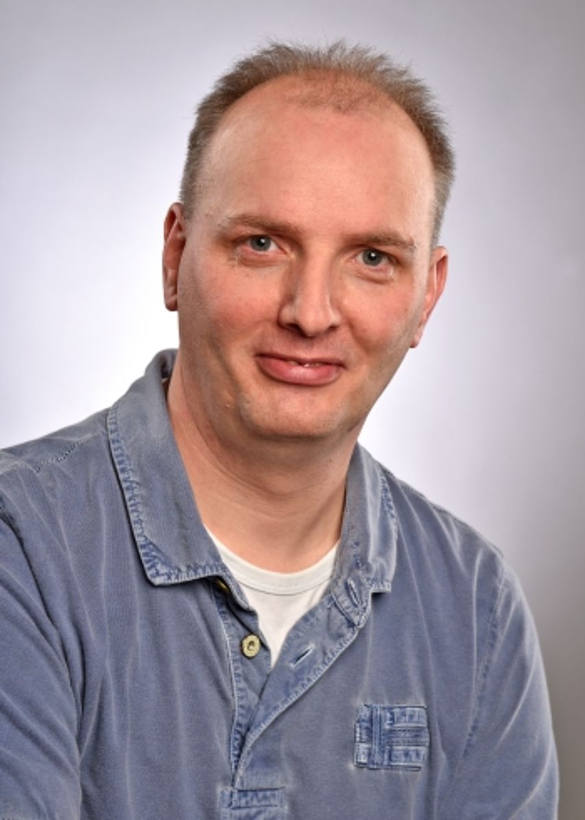 Portrait Michael Kühr Ein Porträtfoto eines freundlich blickenden Mannes mit kurzen, hellbraunen Haaren. Er trägt ein blaues Poloshirt mit einer dezenten Stickerei auf der Brustseite. Der Hintergrund ist in einem neutralen, hellen Grau gehalten und gleichmäßig ausgeleuchtet. Das Bild wirkt bodenständig, sympathisch und professionell.