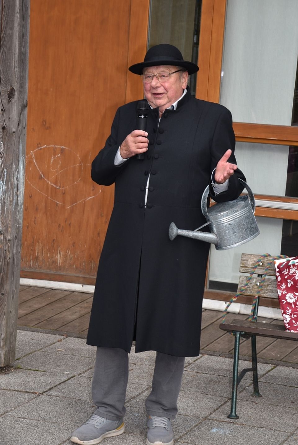 Nahaufnahme des Sebastian-Kneipp-Darstellers im schwarzen Gehrock, der mit Mikrofon und Gießkanne eine Ansprache hält.